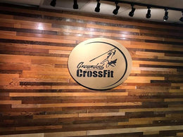 Round custom CrossFit gym metal sign installed on a wood feature wall