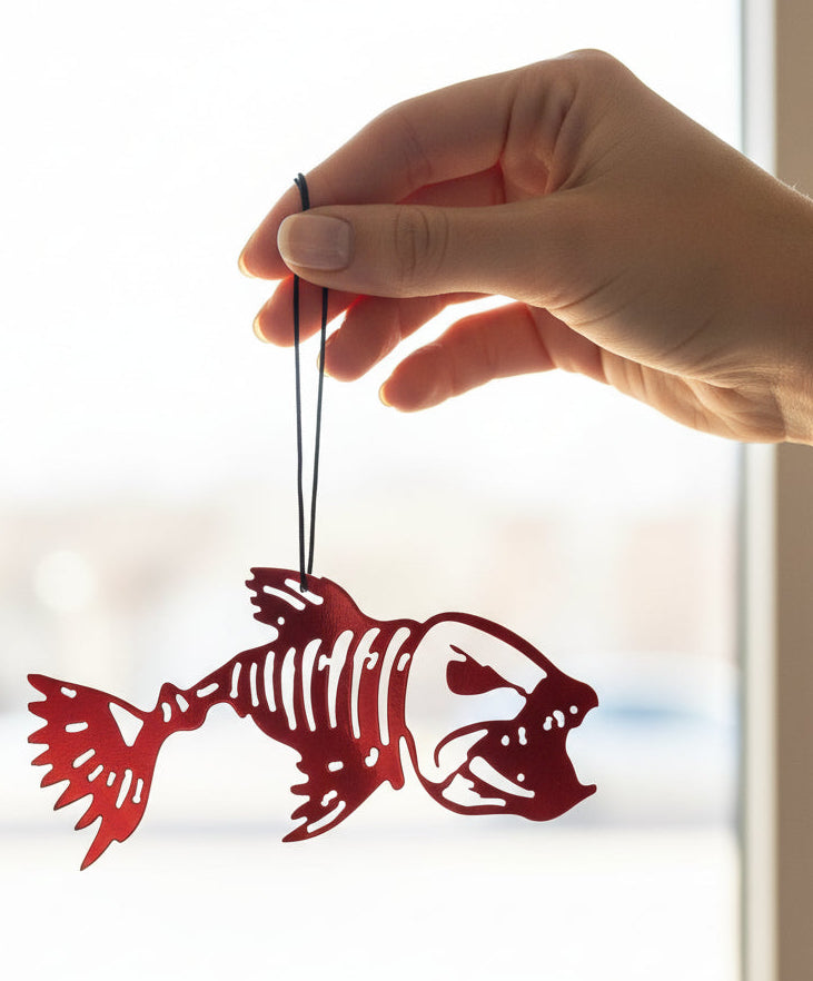 Hand holding a red fish skeleton decoration against a blurred indoor background