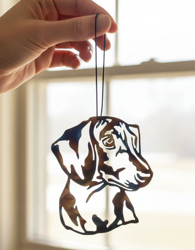 A custom metal art ornament in the shape of a dachshund dog with a multicolored finish, displayed against a reflective surface.