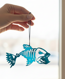 Hand holding a blue fish skeleton decoration against a blurred indoor background
