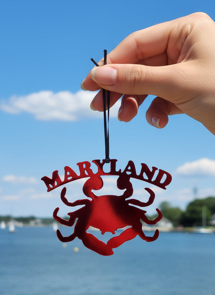 Red Maryland crab ornament held by a hand with a lake and sky background