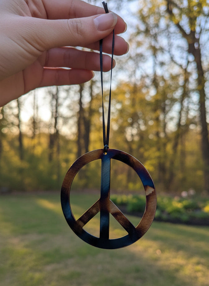 Peace symbol ornament held by a hand with a blurred natural background